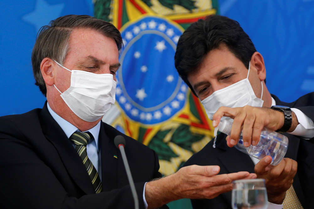 Brazil's President Jair Bolsonaro and Minister of Health Luiz Henrique Mandettas, wearing protective face masks, sanitize their hands during a news conference to announce measures to curb the spread of the coronavirus disease (COVID-19) in Brasilia, Brazil March 18, 2020. REUTERS/Adriano Machado