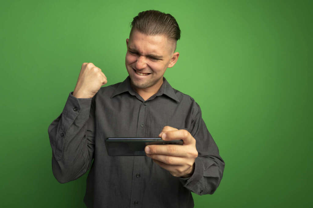 Apostas online: guia completo para iniciantes em esportes e cassino 1 young handsome man grey shirt using gadget clenching fist happy excited rejoicing his success standing green wall